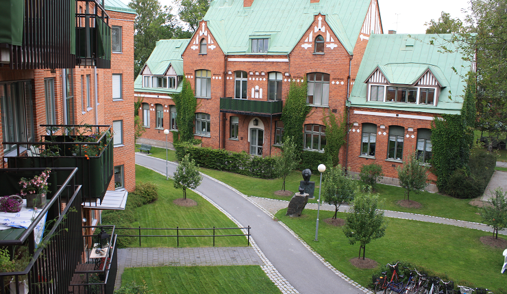 Utsikt mot området på Epidemin i Örebro från en lägenhetsbalkong. Utsikten visar en äldre röd tegelbyggnad med grönt plåtttak och grönytor framför byggnaden