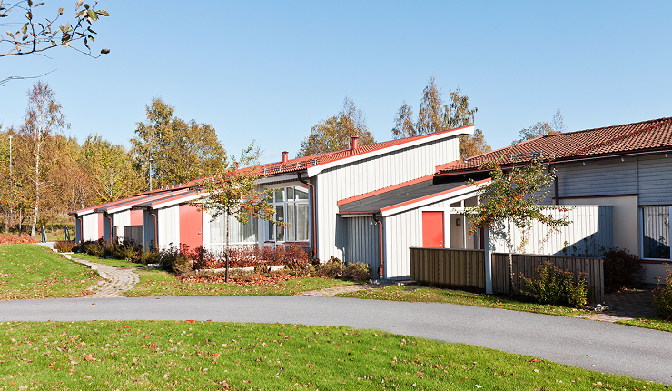 Utsidan av lägenheterna på Bättringsvägen i Karlskoga. Fastigheten består av träpaneler med blå/grå färg, röda dörrar och röda takplattor