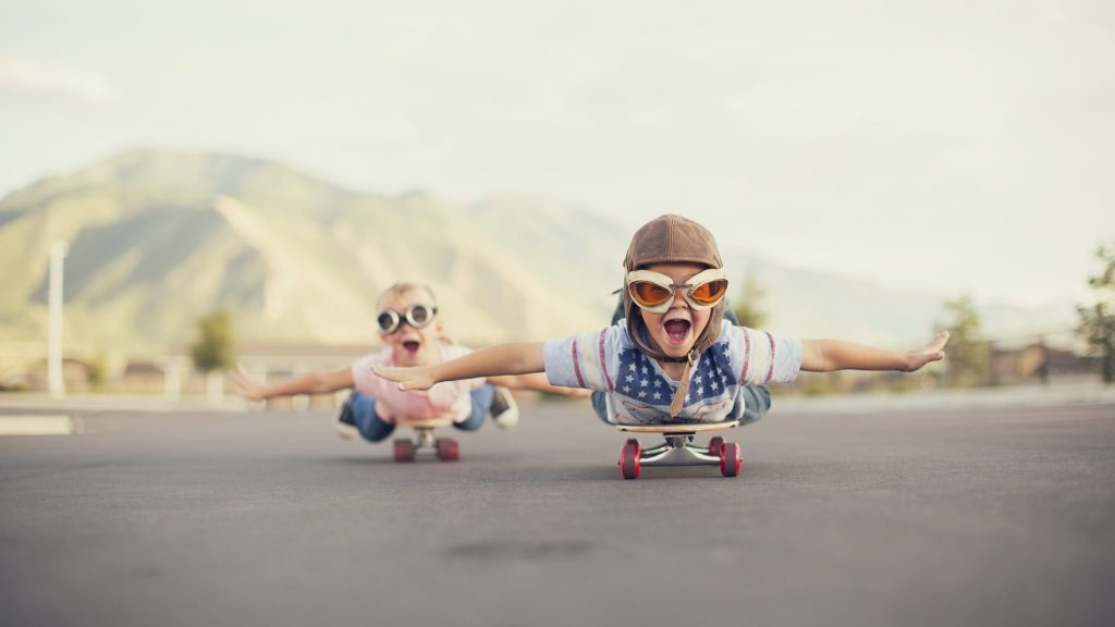 Två barn varav en är en pojke och en är en flicka ligger på två skateboards och håller ut sina armar för att försöka flygga. Dom både är glada och ler och i deras fantasi så flyger dom i luften. Bilden ska symboliseras mod och nytänkande.